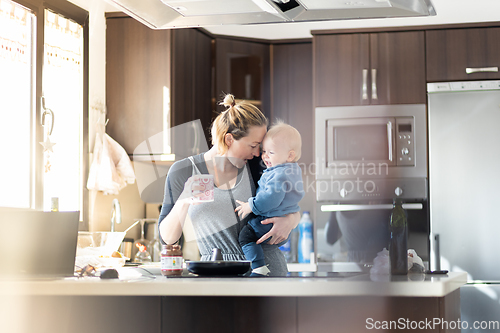 Image of Happy mother and little infant baby boy together making pancakes for breakfast in domestic kitchen. Family, lifestyle, domestic life, food, healthy eating and people concept.