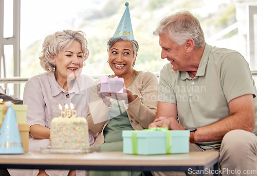 Image of Birthday, senior friends with cake and gift for celebration in living room, smile and candles in retirement. Happiness, old people and party with dessert, surprise and elderly man with women on sofa.