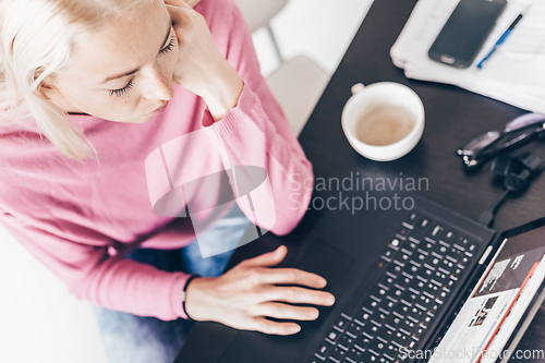 Image of Female freelancer in her casual home clothing remotly working on laptop computer from her home while drinking her morning cup coffee. View from above