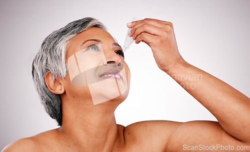 Image of Senior woman, eye drops and body care with cosmetics, product or pharmaceutical against a studio background. Happy mature female person applying liquid to eyes for allergy, treatment or eyesight