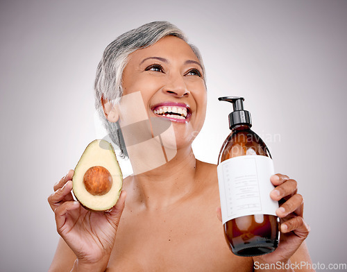 Image of Senior woman, avocado and studio with smile for bottle, product and ideas for nutrition by white background. Mature female model, fruit and thinking for cleaning, beauty or skincare with organic oil