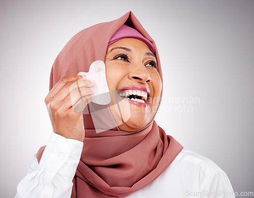 Image of Skin, gua sha stone and a muslim woman closeup in studio on a gray background for beauty. Skincare, smile and natural with a happy mature arab person massaging her face for antiaging treatment