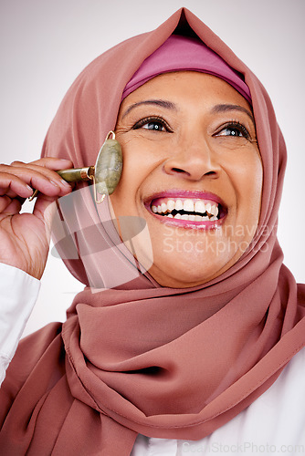 Image of Muslim woman, facial roller and skin care in studio with quartz for dermatology, cosmetics and glow. Happy mature female person with islam hijab, face massage and beauty on a white background