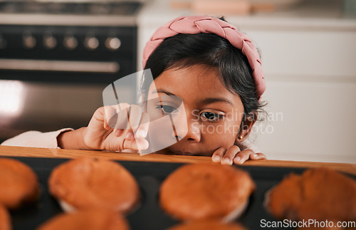 Image of Baking, muffin and a sneaky indian girl in the kitchen of her home to steal a fresh pastry from the counter. Food, children or cooking with a young kid looking naughty at a baked snack closeup