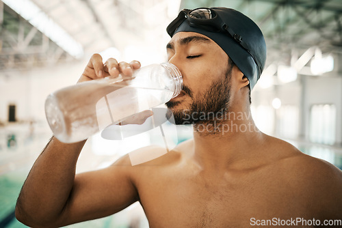 Image of Man, swimmer and drinking water for hydration, exercise or training workout at indoor swimming pool. Active and thirsty male person or athlete with mineral drink for sustainability, fitness or cardio