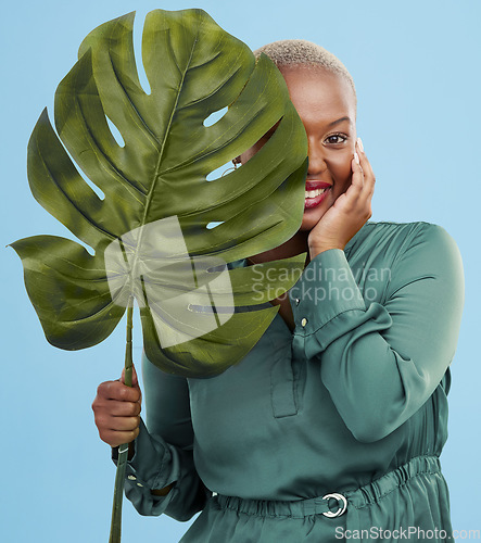 Image of Black woman, monstera leaf and beauty in portrait, natural cosmetics and fashion on blue background. Silk green dress, eco friendly skincare and dermatology, African model glow and plant in studio