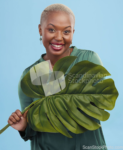 Image of Black woman, monstera leaf and beauty, face with natural cosmetics and fashion on blue background. Silk green dress, eco friendly skincare and dermatology, African model glow and portrait in studio