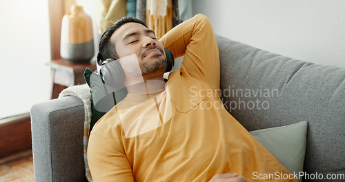 Image of Music, headphones and asian man relax on a sofa with audio, streaming or track in his home. Earphones, radio and male with wellness app in a living room with podcast for resting, nap or day off peace
