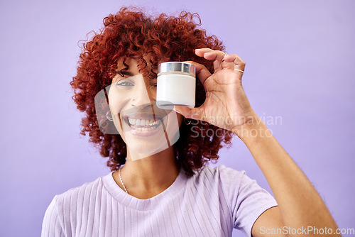 Image of Portrait, beauty and cream for skincare with a woman holding a container in studio on a purple background. Face, smile and promotion of a product or serum for antiaging with a happy young model