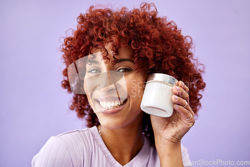 Image of Portrait, beauty and product for skincare with a woman holding a container in studio on a purple background. Face, smile and promotion of a cream or serum for antiaging with a happy young model