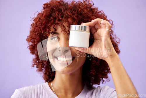 Image of Face, beauty and product for skincare with a woman holding a container in studio on a purple background. Smile, thinking and promotion of a cream or serum for antiaging with a happy young model