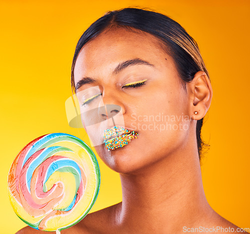 Image of Beauty, lollipop and woman with makeup, candy and sprinkles on her lips on yellow studio background. Person, girl or model with sweet treats, aesthetic and dessert with mockup space or colorful snack