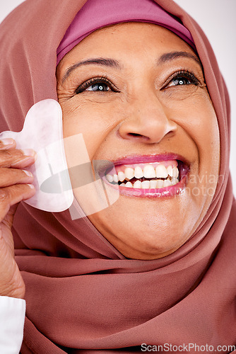 Image of Skincare, gua sha stone and face of muslim woman closeup in studio on a white background for beauty. Spa, smile and natural with a happy mature arab person, massage with stone for antiaging treatment