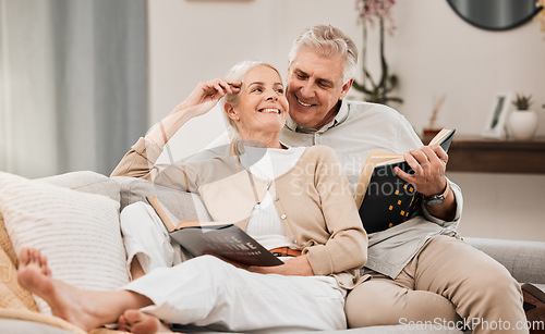 Image of Senior, couple and reading book on a living room sofa with love, smile and retirement in a home. Elderly people, story and lounge on a couch with study for knowledge in a house happy and relax