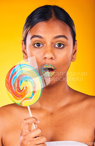 Image of Shock, lollipop and portrait of woman in studio with makeup, cosmetic and face routine. Surprise, beauty and young Indian female model with colorful candy and facial cosmetology by yellow background.