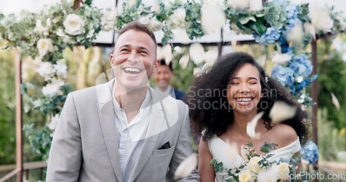 Image of Couple, wedding and walk with flower confetti for event, celebration and outdoor in nature. Girl, happy interracial marriage and floral bouquet in park, holding hands or fist in air, pride or party