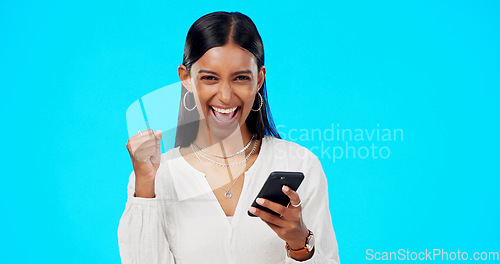 Image of Winner woman, phone and studio with fist celebration, portrait and excited for prize by blue background. Girl, trader and smartphone with cheers, success or goals with investment, fintech or stocks