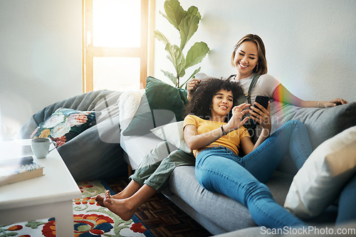 Image of Women, lgbt couple and smartphone on couch, living room and relaxing together for quality time, videos and bonding. Social media apps, indoors and smiling while streaming online, memes and cellphone