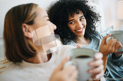 Image of Coffee, happy and lesbian couple on bed in conversation for bonding and relaxing together. Smile, rest and interracial lgbtq women laughing, talking and drinking latte in bedroom of modern apartment.