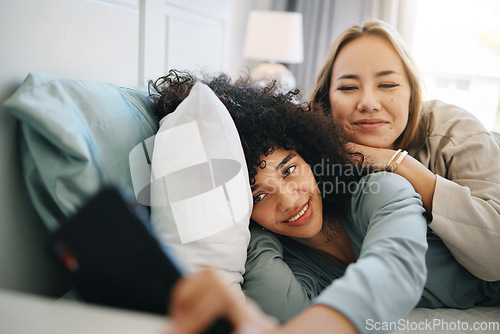 Image of Cellphone, relax and young lesbian couple on a bed networking on social media, mobile app or the internet. Happy, technology and interracial lgbtq women scroll on cellphone in bedroom at apartment.