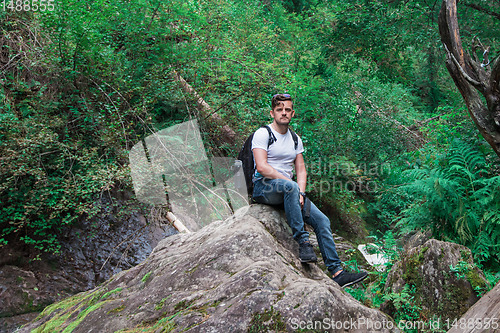 Image of Man traveler with backpack sitting on rock in the forest.