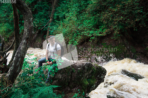 Image of Man traveler with backpack sitting on rock in the forest.