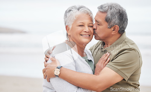 Image of Senior couple, kiss and love at beach for holiday, vacation and tropical travel in retirement. Happy man, elderly woman and hug of affection at ocean for trust, support and loyalty to partner on date