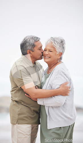 Image of Senior couple, kiss or hug on beach with smile, embrace and enjoying for retirement, happy or love. Senior citizen, romance and lovers with bond, happiness and vacation for travel, anniversary or fun