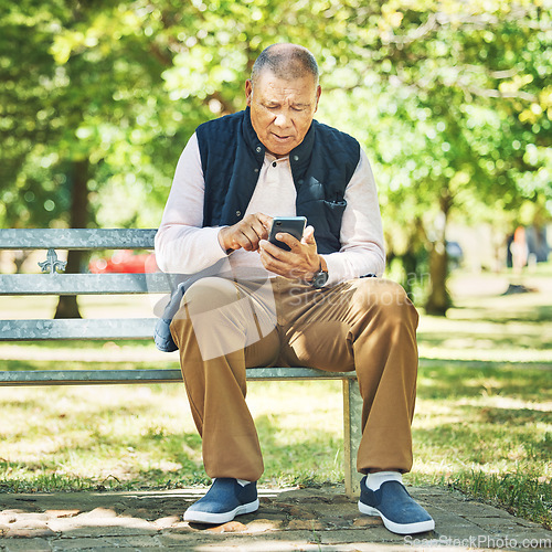 Image of Senior man, typing and phone on park bench, learning and network with technology online, nature and outdoor. Elderly person, message and email on smartphone, digital and contact in retirement