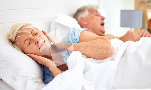 Image of Snoring, problem and woman with frustrated with noise, sound or husband sleeping in bed with wife. Elderly, couple and man snore in sleep in retirement home bedroom and lady with hands on ears