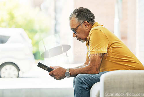 Image of Serious, mature man and reading bible in home, praying and thinking in living room on sofa. Person, holy book and gospel in house for learning religion, studying and Christian worship in retirement