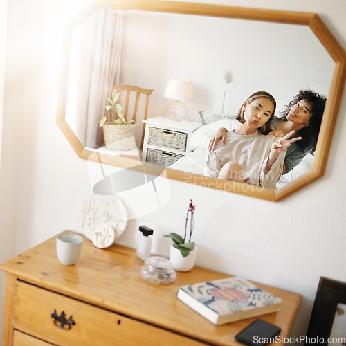 Image of Happy lesbian couple in bedroom with mirror, peace sign icon and relax together in apartment. Queer love, smile and reflection of lgbt women on bed with emoji hand gesture, trust and support in home.