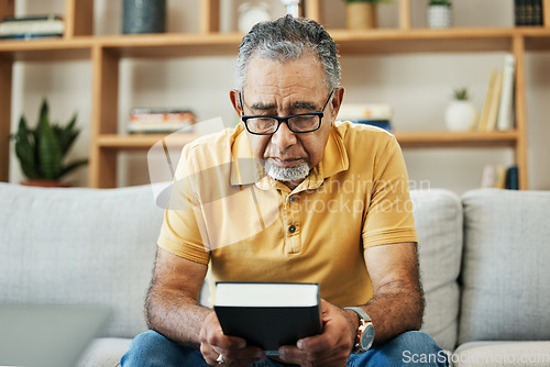 Image of Mature, man and bible by thinking in home, alone and sadness of memory in living room of thoughts. Elderly, person or grandfather on sofa with hand, holding and book for religion, church or practice