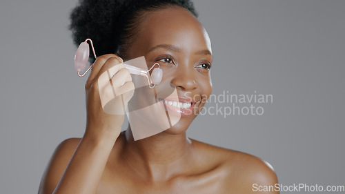 Image of Facial roller, woman and smile in face massage in skincare or beauty, health and wellness or dermatology. Happy black person, skin and cosmetics with glow, care and tool in studio by gray background