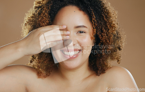 Image of Portrait, funny or happy woman with natural beauty dermatology for wellness in studio with smile. Hand, eye cover or biracial female person laughing with skincare, pride or glow on brown background