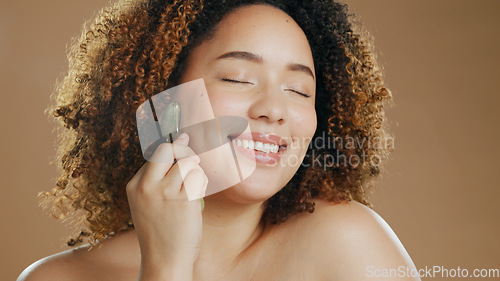 Image of Happy woman, relax or jade roller in studio for face with anti aging product or facial tool on brown background. Smile, beauty or confident girl model with cosmetics for wellness or natural skincare