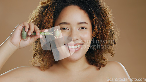 Image of Happy woman, portrait or jade roller in studio with anti aging product or facial tool on brown background. Smile, beauty or proud biracial girl model with cosmetics for wellness or natural skincare