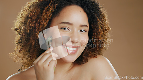 Image of Portrait of happy woman, smile or jade roller in studio with anti aging product or facial tool to relax. Brown background, results or healthy model with cosmetics for wellness or natural skincare