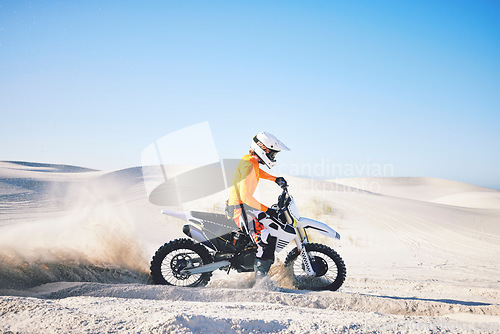 Image of Extreme sport, motorcycle and athlete with sand by wheels with pride, skill and adrenaline rush. Biker, sunshine and dust with blue sky in fun, fitness and achievement in speed, race and lens flare