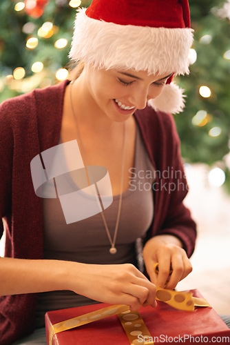 Image of Christmas, present and happy young woman opening a box by the tree in celebration of holidays. Happiness, excited and girl from Canada with xmas gift wearing festive, fun and traditional hat at home.