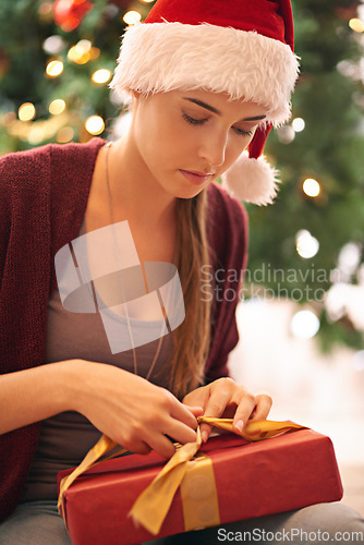 Image of Christmas, gift and woman on floor in living room on xmas eve, content and calm while wrapping ribbon. Festive, holiday and girl open present box in celebration of traditional holiday in her home