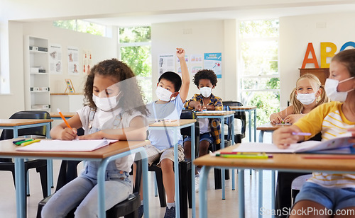 Image of Young kids learning in classroom after covid pandemic, wearing protective face masks. Little children sitting in school with raised arm to ask questions and studying for their education