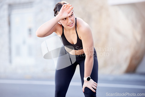 Image of Fitness, tired and sweat with a sports woman wiping her brow after running outdoor in the city for cardio. Road, exercising and training with a female runner or athletr sweating during endurance