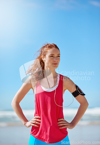 Image of Runner woman, beach and sky with earphones for music, workout motivation and training by ocean. Athlete girl, exercise and running for wellness by sea waves with focus for fitness, health and outdoor