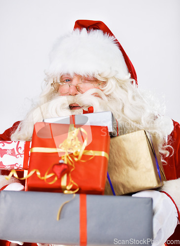 Image of Wink, Christmas gifts and portrait of Santa Claus in studio on white background. Xmas, costume and man with glasses holding pile of presents for happy December holiday celebrations or festive party