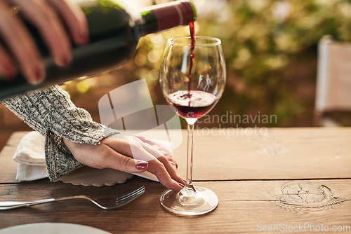 Image of Glass, bottle and hand of woman pouring wine at a table, calm and content while enjoying free time on a patio. Red wine, hands and lady relax with luxury drink, enjoy a relaxing weekend alone at home