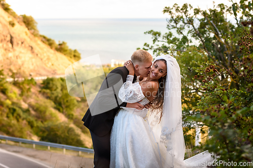 Image of Happy newlyweds kiss against the backdrop of a beautiful mountain landscape, the girl fervently turns away from the guy