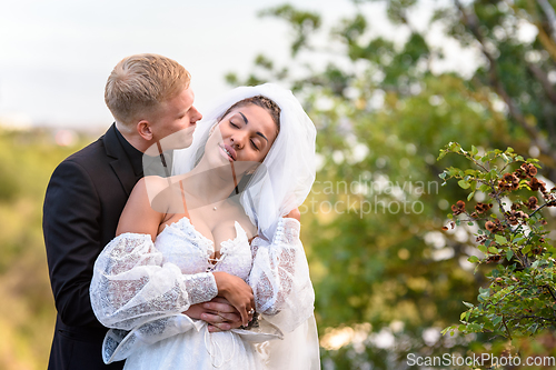 Image of Happy newlyweds hug against the backdrop of a beautiful mountain landscape, the guy kisses the girl who has closed her eyes