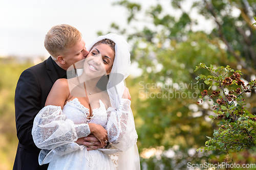 Image of Happy newlyweds hug against the backdrop of a beautiful mountain landscape, the guy kisses the girl