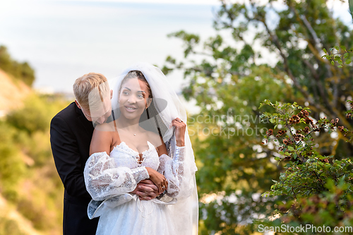 Image of Newlyweds hug against the backdrop of a beautiful landscape, the guy kisses the shoulder of a girl who has a happy look